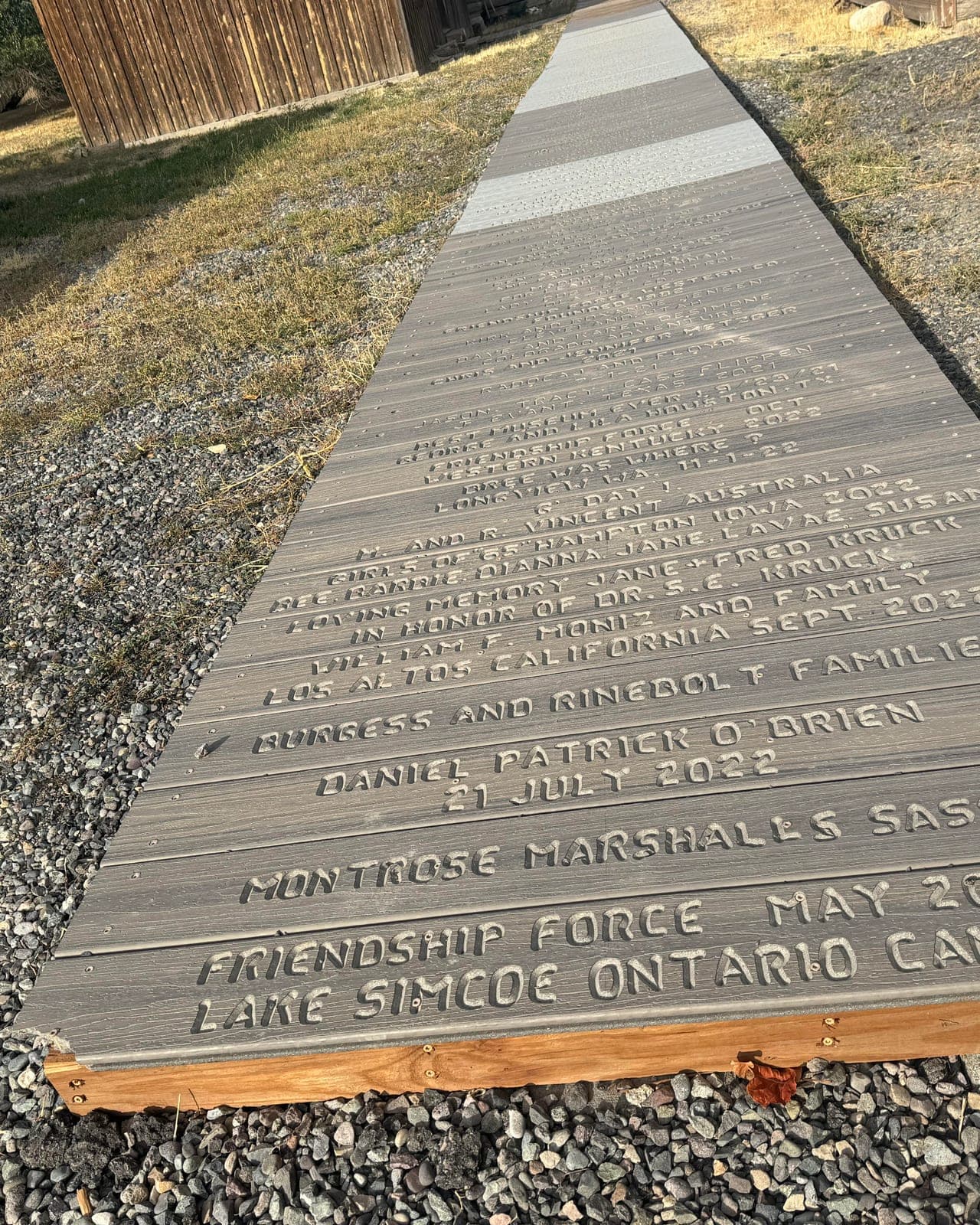 Boardwalk planks carved with visitors’ names, hometowns and dates, running along a gravel path
