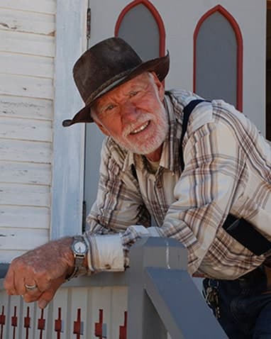 Rich Fike in a cowboy hat, leaning on the porch rail of the white church