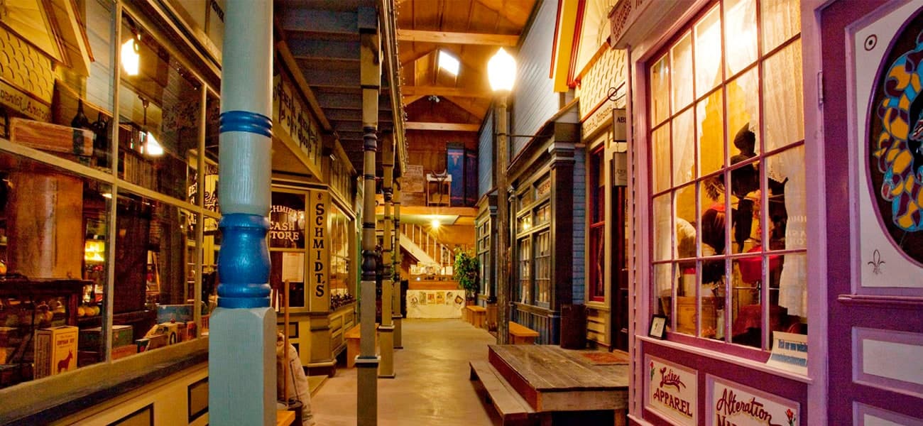 The indoor Main Street boardwalk, lit by street lamps, with Schmidt’s Cash Store and the Ladies Apparel shop