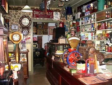 Inside the old mercantile: shelves of tins and bottles, wall clocks and a red coffee grinder on the counter