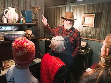A docent in a cowboy hat points out objects in a period room to a group of children
